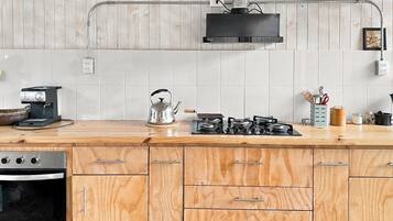 A kitchen with a wooden countertop, a stove, a kettle, and a dishwasher.