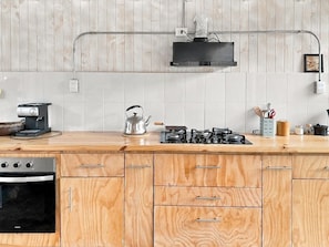 A kitchen with a wooden countertop, a stove, a kettle, and a dishwasher.