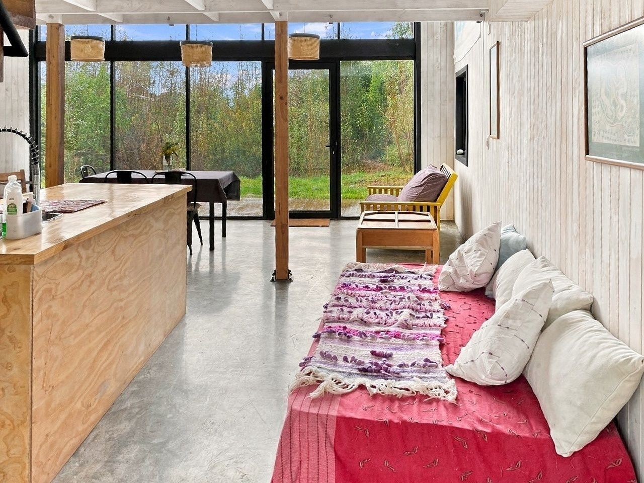 A modern interior with a wooden bar, a red bed with pillows, and a view of the outdoors.