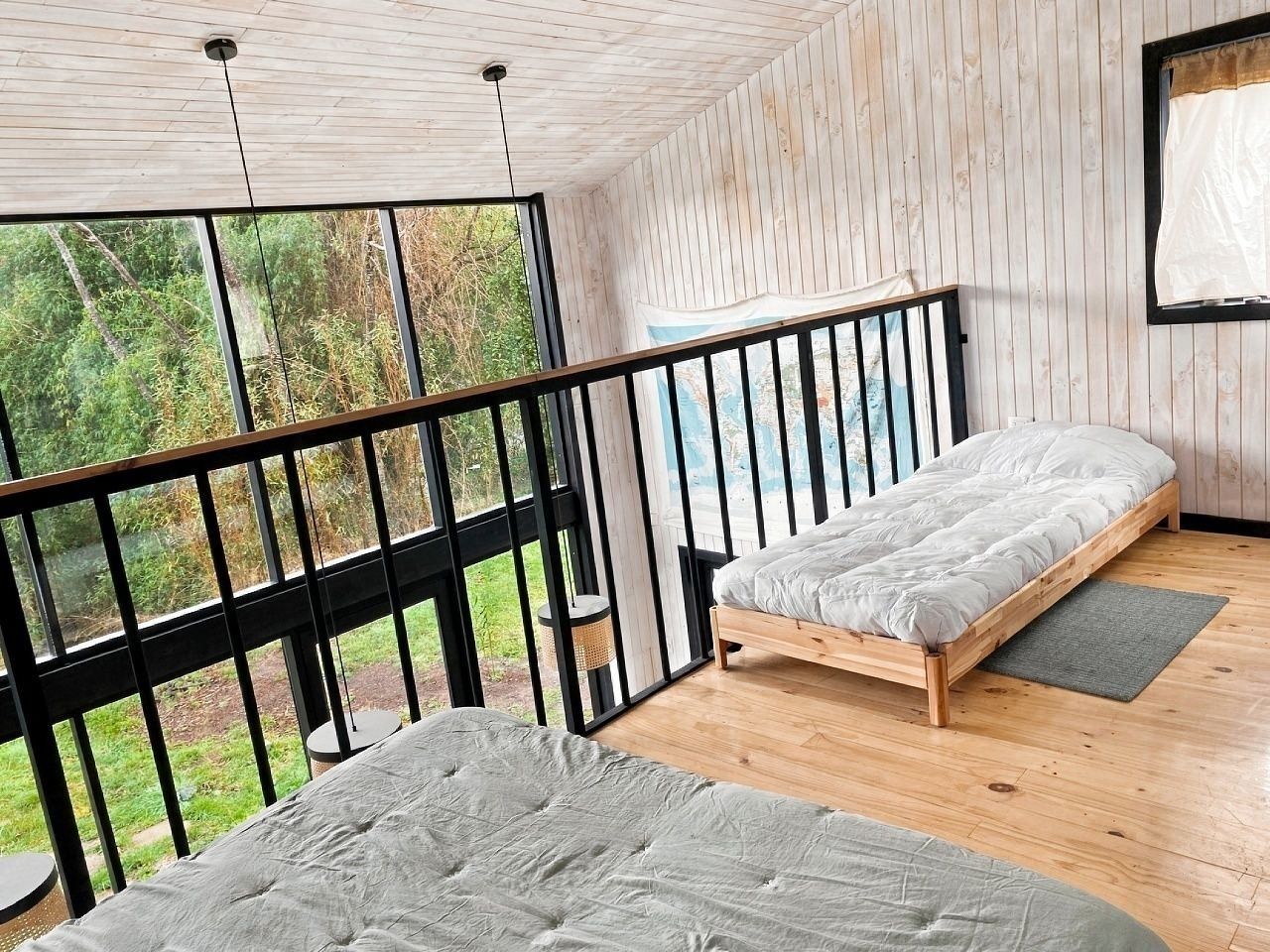 Un dormitorio con cama de madera, ventana con vistas a la vegetación y balcón con barandilla.