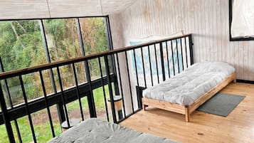Un dormitorio con cama de madera, ventana con vistas a la vegetación y balcón con barandilla.
