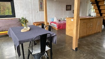 Un'area pranzo con tavolo e sedie, un letto con coperta rossa e un armadio in legno.