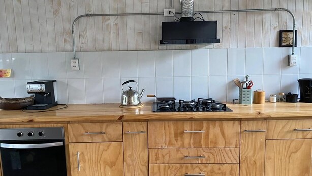 A kitchen with wooden cabinets, a gas stove, a kettle, and a dishwasher.