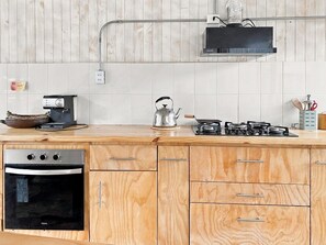 Una cocina con armarios de madera, horno empotrado, cocina a gas y hervidor sobre la encimera.
