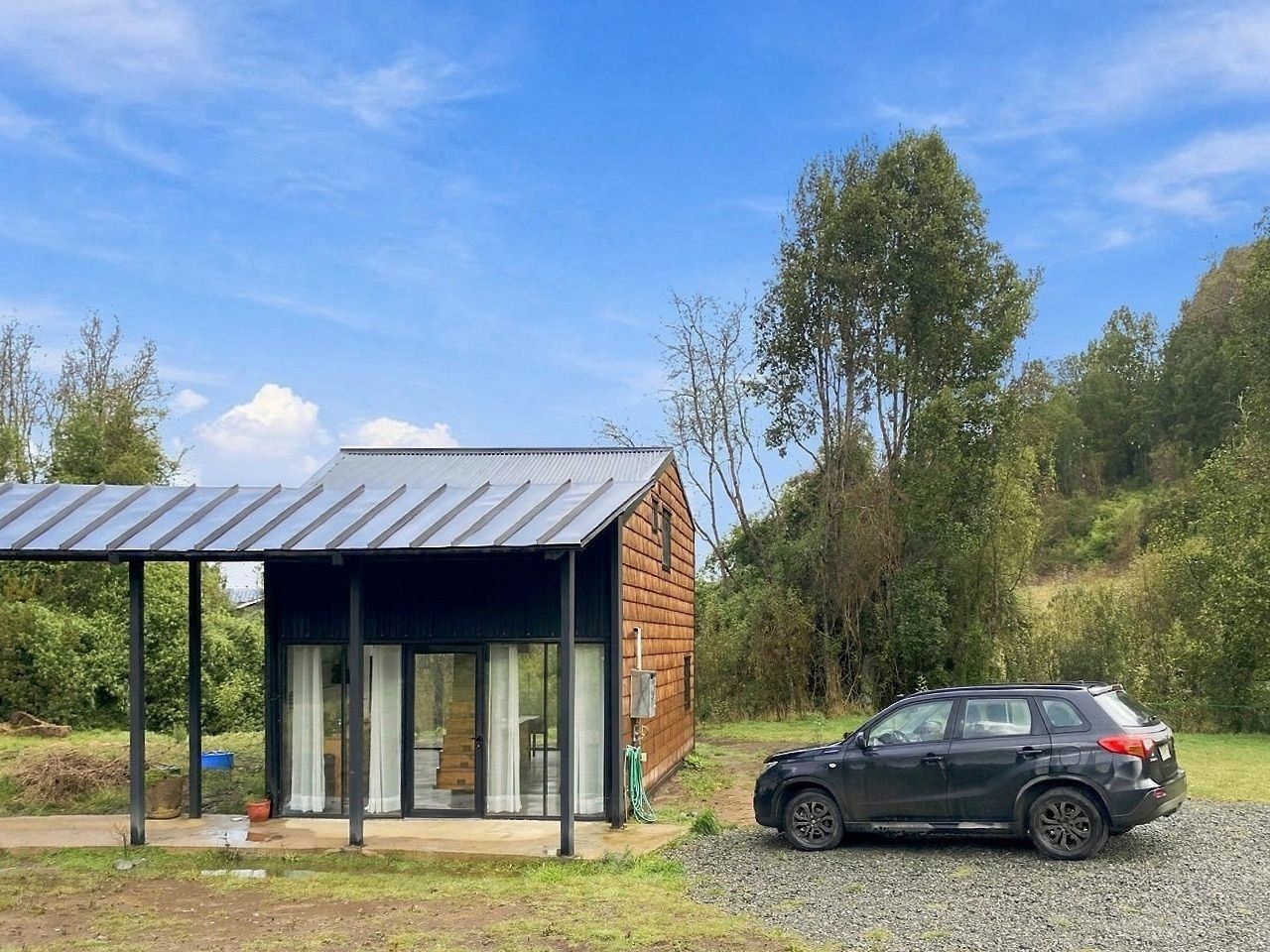 Una moderna baita in legno con veranda coperta e un'auto parcheggiata davanti.