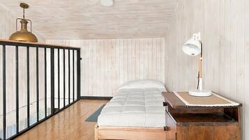 Quarto com cama, escrivaninha com abajur, piso de madeira e varanda com corrimão.