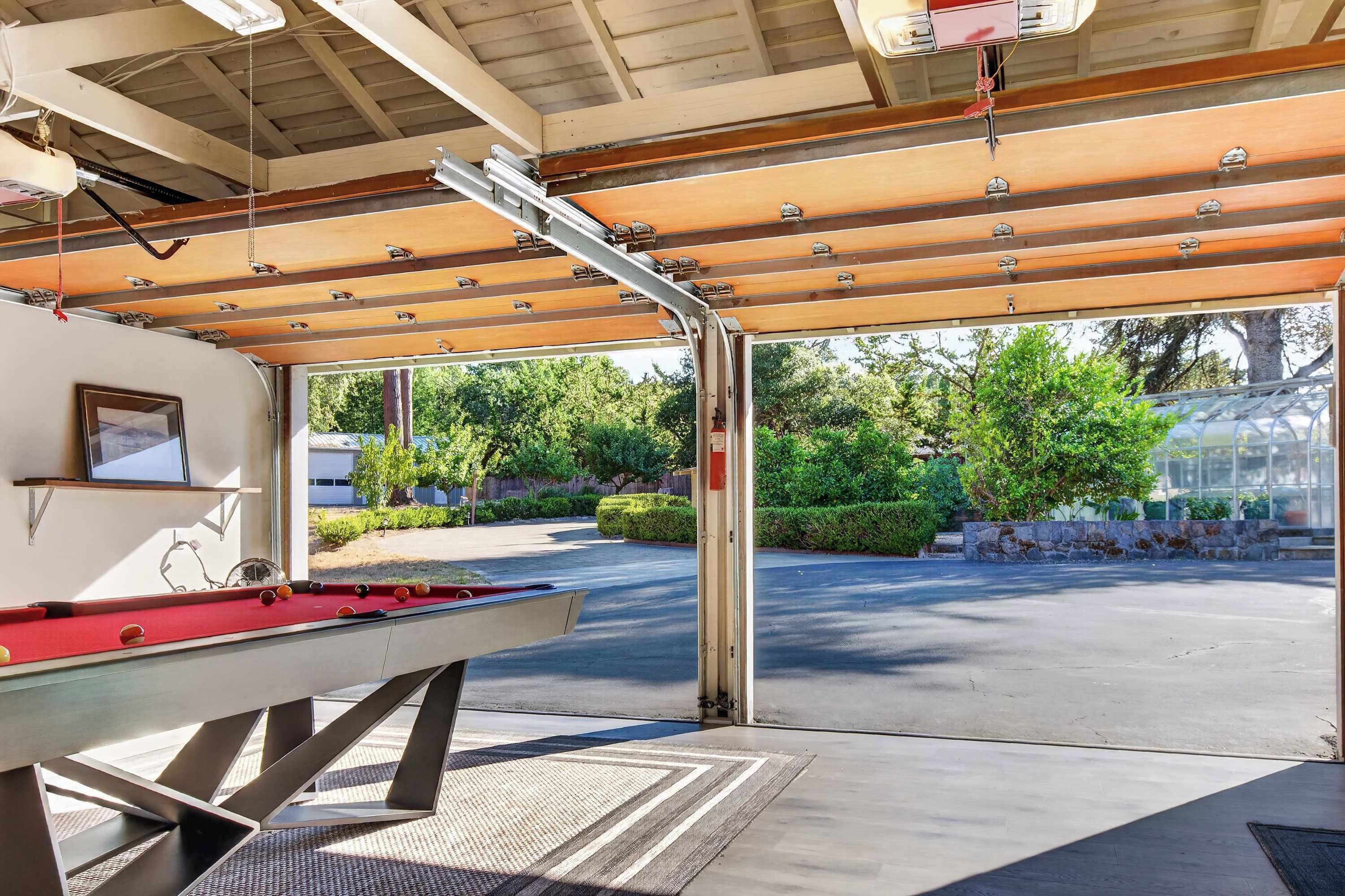 Une table de billard placée sous une zone abritée, avec vue sur un parking et sur la verdure environnante.