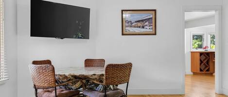 A dining area with a table and four wicker chairs, a flat-screen TV mounted on the wall, and a framed picture above the table.