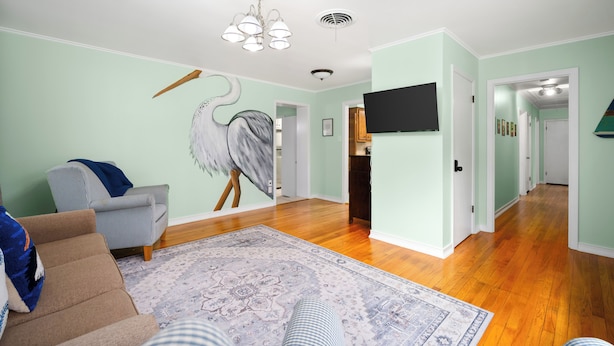 A living room with a large painting of a bird, a sofa, a patterned rug, and a television on the wall.