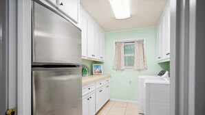 A kitchen with white cabinets, a stainless steel refrigerator, a washing machine, and a window with a curtain.