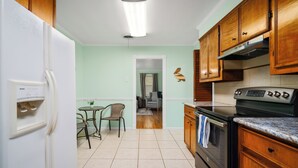 A kitchen with a refrigerator, stove, wooden cabinets, and a dining area with a table and chairs.