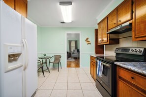 Une cuisine équipée d’un réfrigérateur, d’une cuisinière, de meubles de rangement en bois et d’un coin repas avec une table et des chaises.