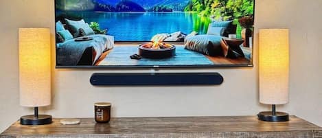 A television mounted on a wall with a scenic landscape image, flanked by two lamps on a wooden cabinet below.