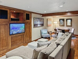 A living room with a large flat-screen TV, a gray sectional sofa, a blue armchair, and a dining area with a round table and chairs. - Aspen View Lodge | Hot Tub & Game Room (Breckenridge)