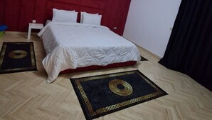 Une chambre avec un lit, une tête de lit rouge, un luminaire blanc au plafond et un rideau noir.