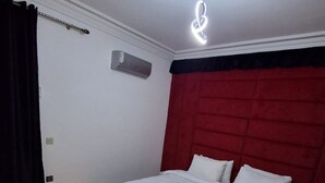 Une chambre à coucher avec un lit, une tête de lit rouge, un appareil de climatisation et un tapis aux motifs noirs et dorés.