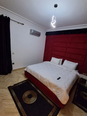 Ein Schlafzimmer mit einem Bett, einem roten Kopfteil, einer Klimaanlage und einem Teppich mit schwarz-goldenem Muster.