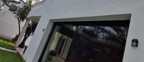 Un edificio moderno con un gran ventanal, paredes exteriores blancas y un pequeño jardín.