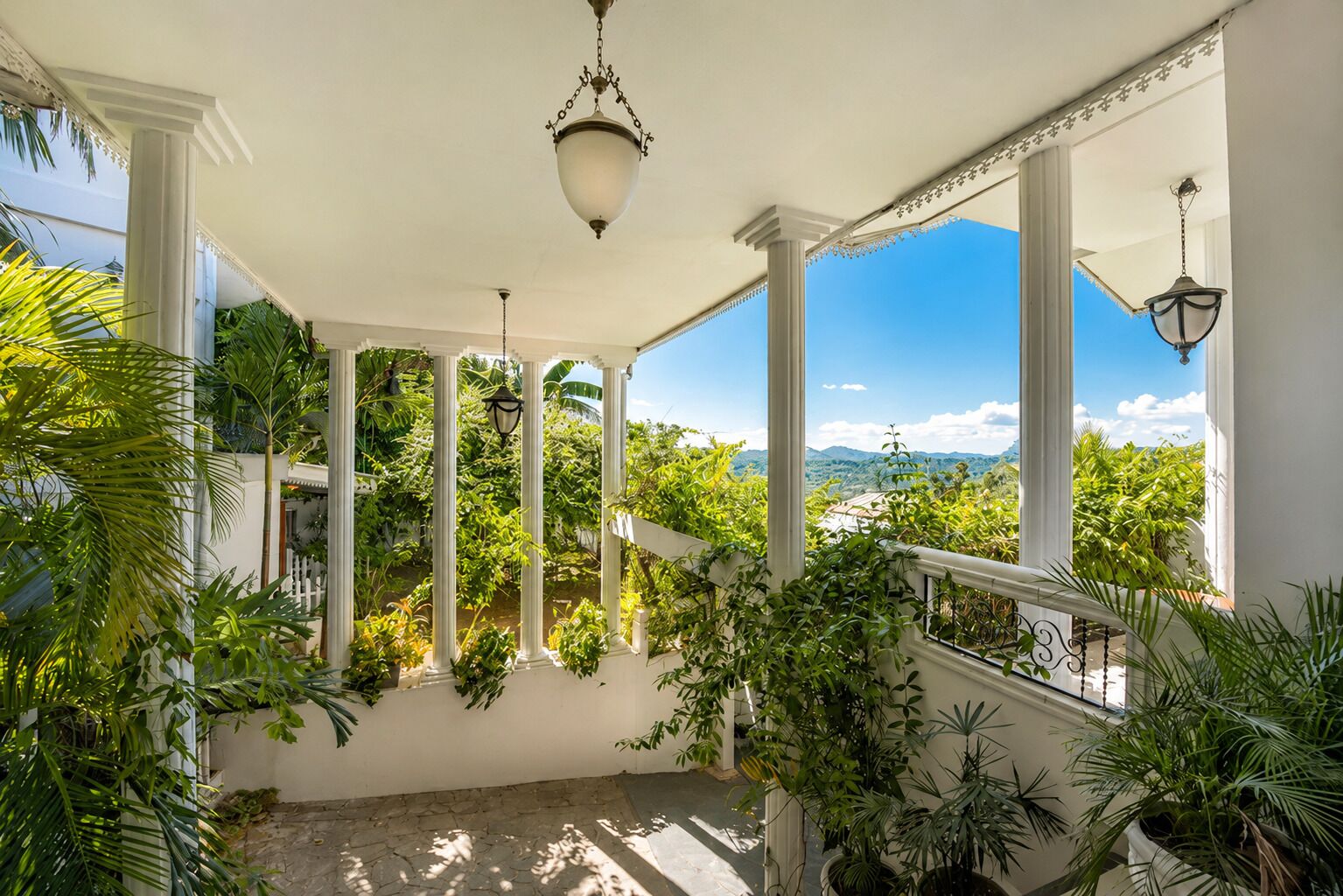A covered outdoor area with columns, potted plants, and a view of the landscape.