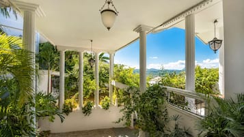 A covered outdoor area with columns, potted plants, and a view of the landscape.