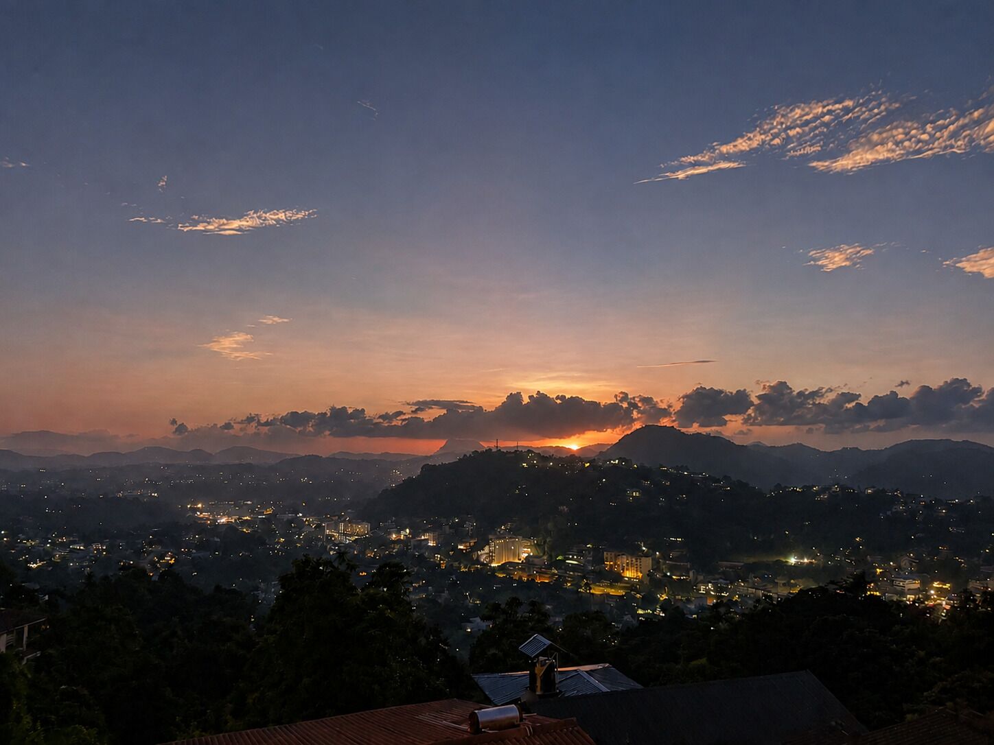 A nighttime cityscape with a sunset, mountains in the background, and a view of a residential area.