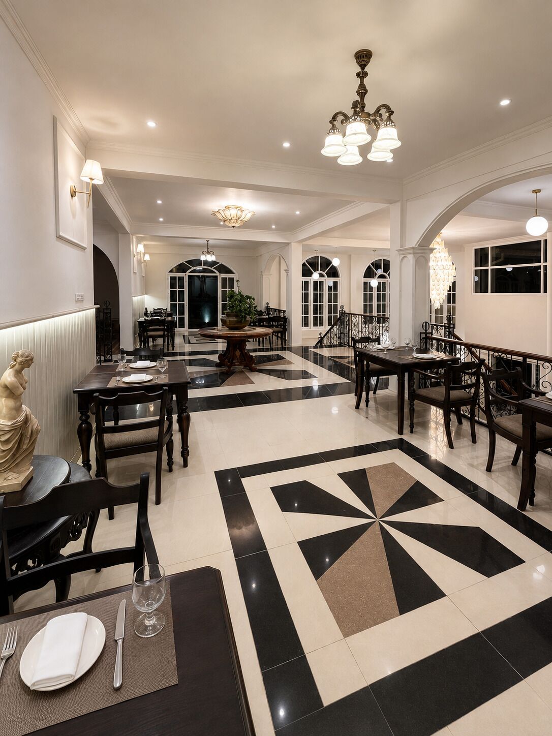 Une salle à manger spacieuse avec un sol carrelé en noir et blanc, de magnifiques lustres et une table ronde placée au centre.