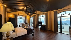 Un dormitorio amplio con una cama grande, un escritorio y una televisión. Varias ventanas ofrecen vistas al exterior.