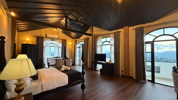 Un dormitorio amplio con una cama grande, un escritorio y una televisión. Varias ventanas ofrecen vistas al exterior.