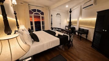 A hotel room with a bed, bedside table, lamp, and a view of the city at sunset.
