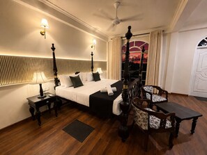A hotel room with a four-poster bed, a desk with a lamp, a chair, and a view of the sunset through a window. - ceylon Breeze kandy (Kandy)