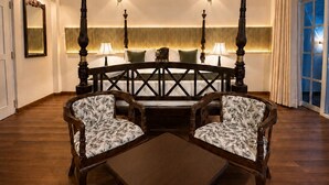 A room with a round table, four chairs, a ceiling fan, wall sconces, and a large window with curtains.