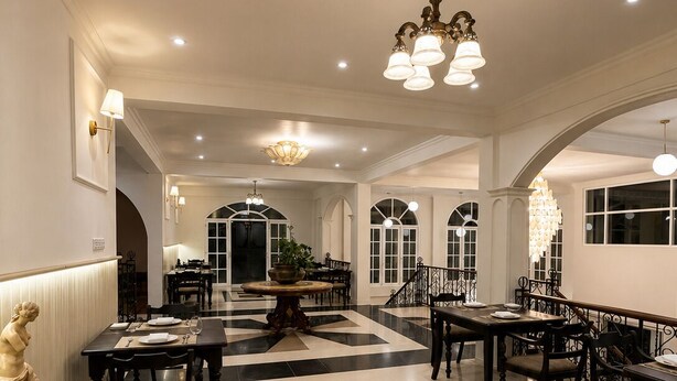 A spacious dining area with multiple tables and chairs, a central chandelier, and a patterned floor.