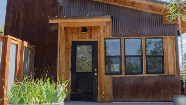 A two-story building with a wooden exterior, a front door, and large windows. - Stunning Desert Sanctuary - Tiny House with Mesa Verde Views & Starry Nights (Dolores)