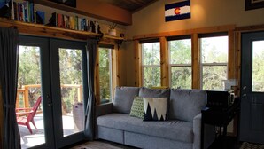 A cozy living room with a grey sofa, a coffee table, and a bookshelf. - Stunning Desert Sanctuary - Tiny House with Mesa Verde Views & Starry Nights (Dolores)
