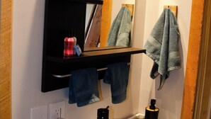 A bathroom with a white sink, a mirror above it, and a shelf with towels and toiletries. - Stunning Desert Sanctuary - Tiny House with Mesa Verde Views & Starry Nights (Dolores)