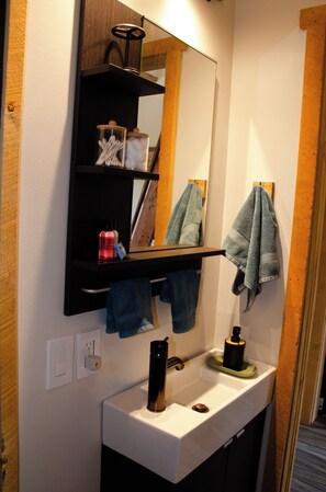 A bathroom with a white sink, a mirror above it, and a shelf with towels and toiletries. - Stunning Desert Sanctuary - Tiny House with Mesa Verde Views & Starry Nights (Dolores)