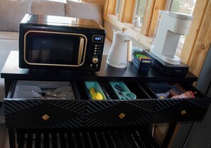 A kitchen counter with a microwave, coffee maker, and a drawer with utensils.