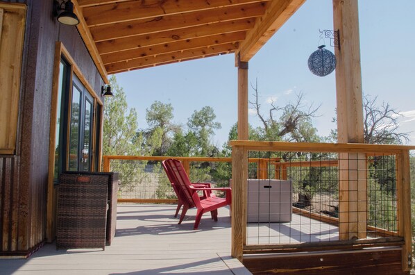 A wooden deck with a red chair and a small table, overlooking a fenced area with trees.
