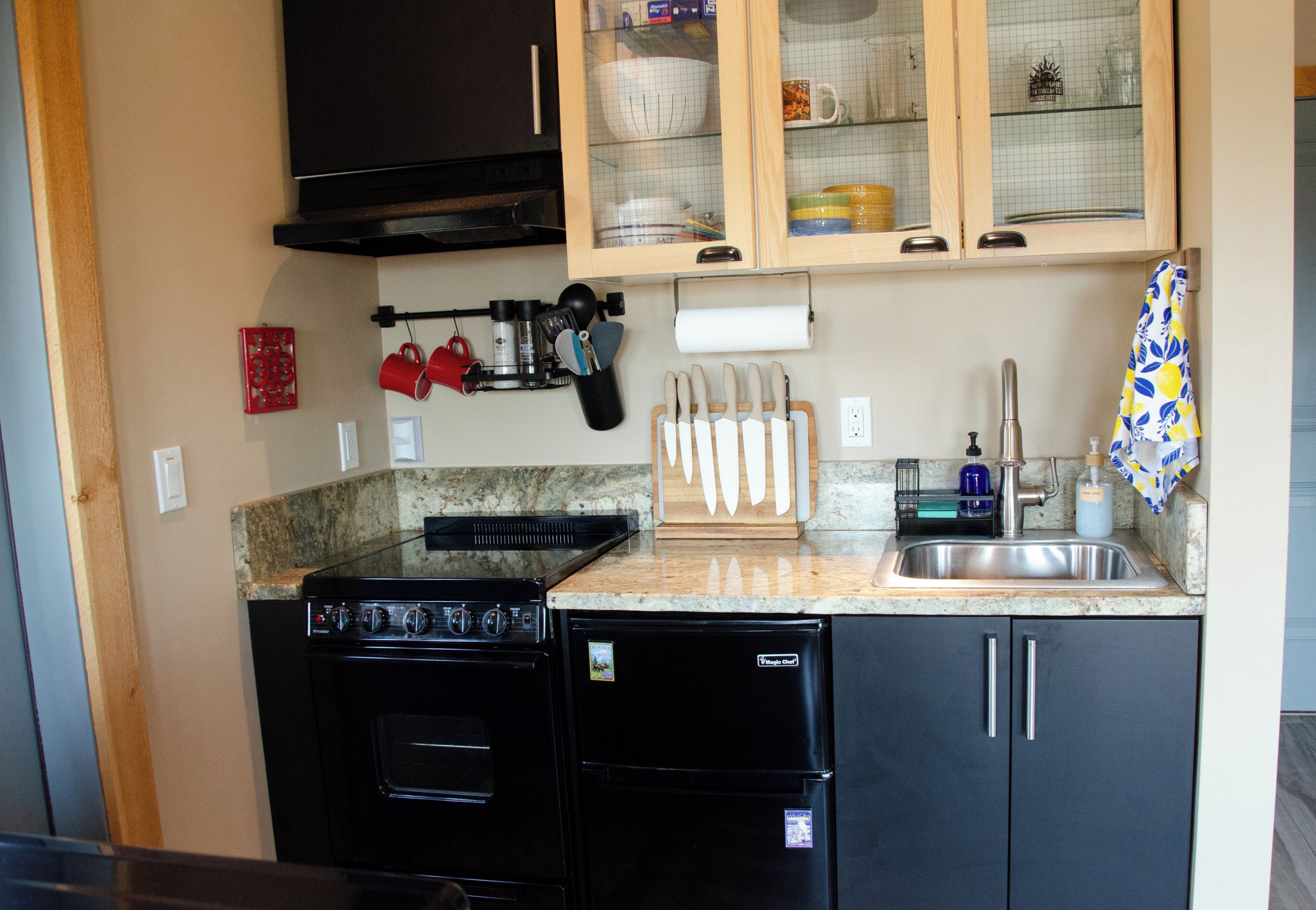 A compact kitchen with a stove, oven, and dishwasher. There are cabinets above the counter and a sink with a faucet.