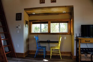 Una habitación con techo de madera, una ventana, dos sillas, un escritorio y un televisor.