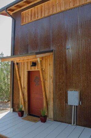 A wooden building with a red door, a porch with potted plants, and a mailbox.