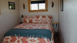 A bedroom with a bed, a window, a nightstand, and a wall-mounted lamp. - Stunning Desert Sanctuary - Tiny House with Mesa Verde Views & Starry Nights (Dolores)