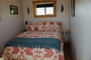 A bedroom with a bed, a window, a nightstand, and a wall-mounted lamp. - Stunning Desert Sanctuary - Tiny House with Mesa Verde Views & Starry Nights (Dolores)