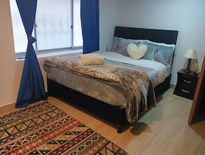 Ein Schlafzimmer mit einem Bett, einem Nachttisch, einer Lampe und einem Fenster mit Vorhängen.