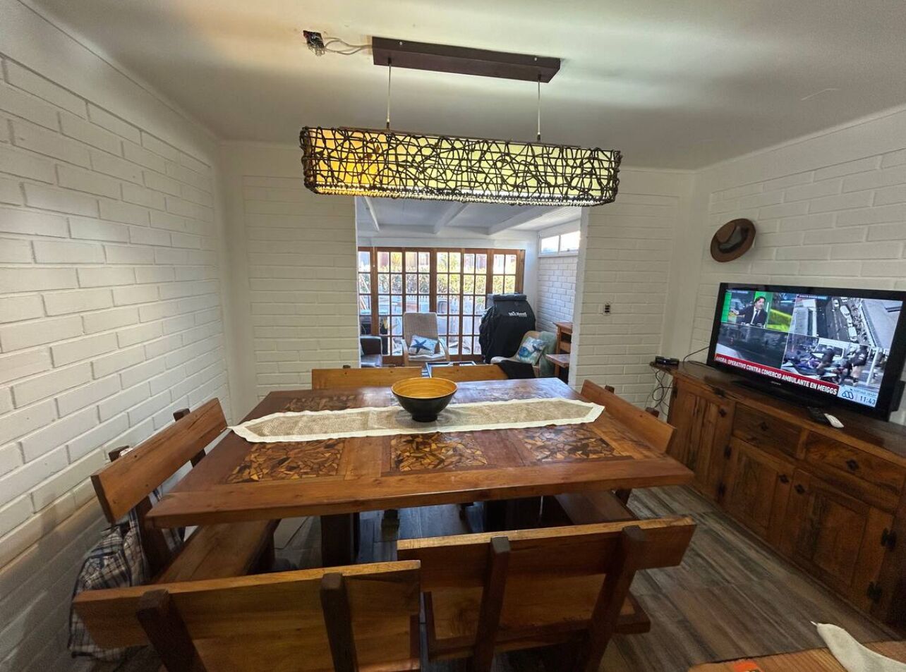 A dining area with a wooden table, chairs, a central bowl, and a television on a cabinet.