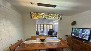 A dining area with a wooden table, chairs, a central bowl, and a television on a cabinet. - Beautiful house in a condominium complex with a pool (Bahía Inglesa)