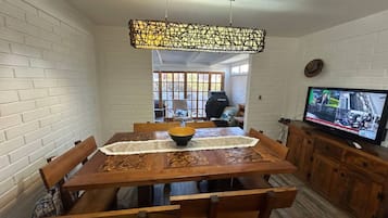 A dining area with a wooden table, chairs, a central bowl, and a television on a cabinet.