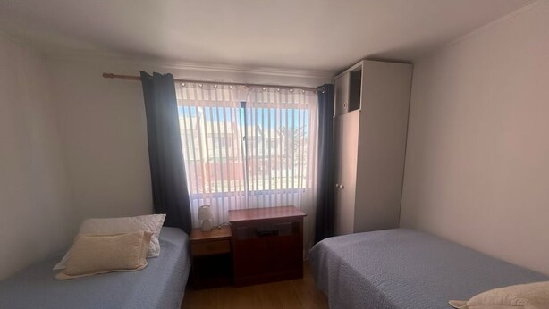A small, single-room accommodation with two beds, a desk, and a window with curtains. - Beautiful house in a condominium complex with a pool (Bahía Inglesa)