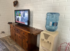 A room with a wooden cabinet, a television displaying news, and a water dispenser.