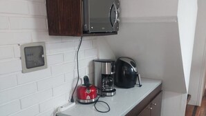 A compact kitchen with a microwave, coffee maker, and kettle on the counter, a red wire basket, and a white brick wall. - Beautiful house in a condominium complex with a pool (Bahía Inglesa)